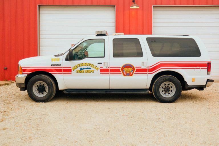 A white and red emergency vehicle labeled "weathersville fire dept." parked in front of a red building with a gravel ground.
